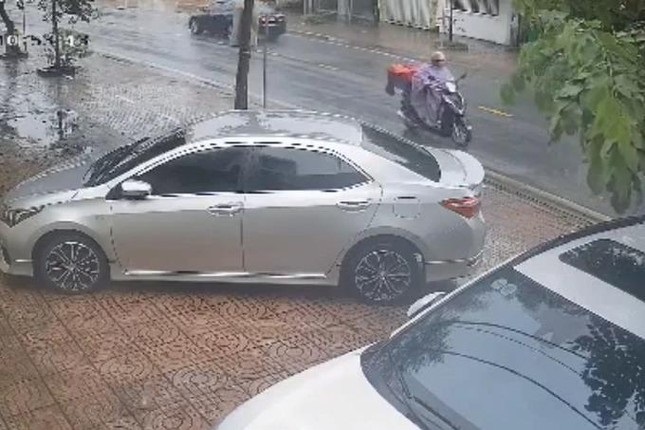 Hình ảnh người phụ nữ mặc áo mưa đi xe máy lưu thông trên đường, đi đúng làn đường quy định trước khi bị ô tô đi ngược chiều tông trúng (Ảnh cắt từ clip do camera an ninh ghi lại).